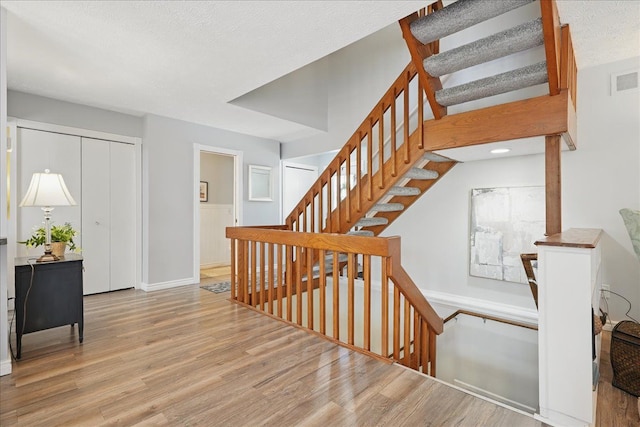 stairs featuring a textured ceiling, baseboards, visible vents, and wood finished floors