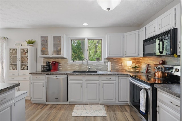 kitchen featuring a sink, dark countertops, light wood-style floors, white cabinets, and appliances with stainless steel finishes