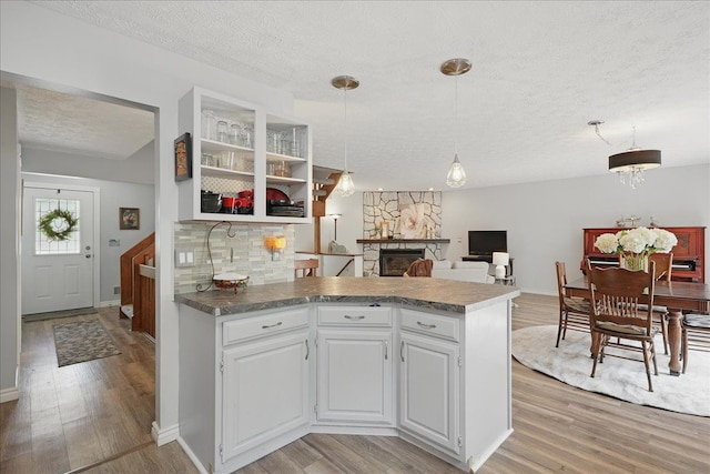 kitchen with a stone fireplace, a peninsula, light wood-style flooring, and a textured ceiling