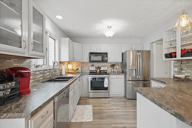 kitchen with a sink, light wood finished floors, white cabinets, dark countertops, and appliances with stainless steel finishes