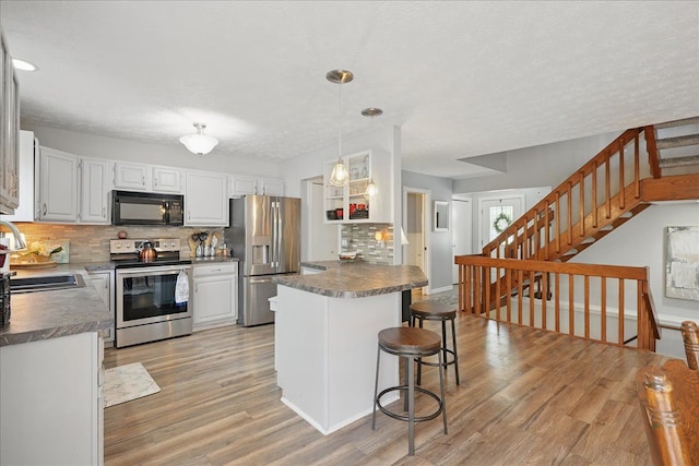 kitchen with a sink, stainless steel appliances, a kitchen breakfast bar, light wood-style flooring, and decorative backsplash