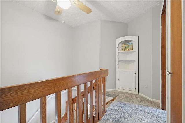 corridor featuring baseboards, carpet flooring, an upstairs landing, and a textured ceiling