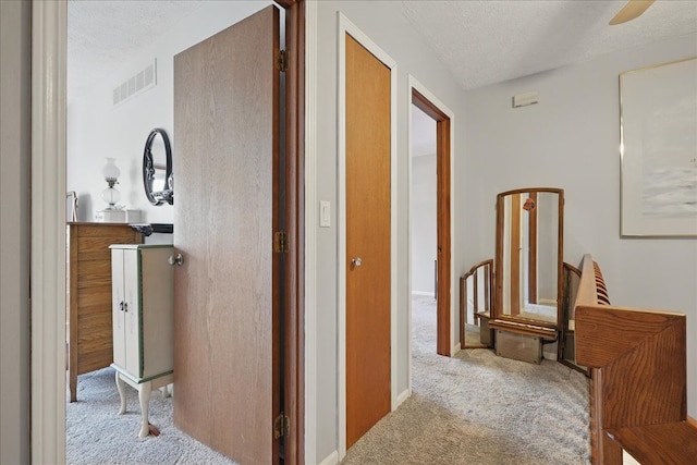 hall with a textured ceiling, visible vents, and carpet floors