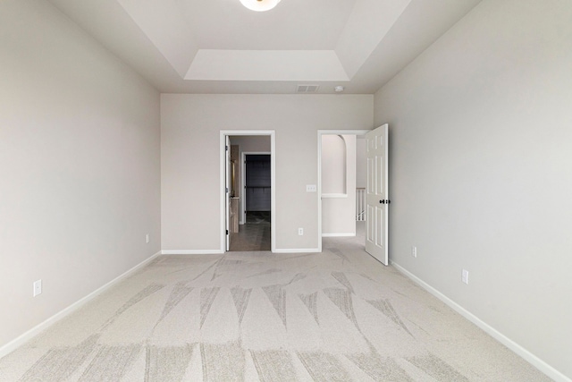 unfurnished bedroom featuring visible vents, baseboards, a walk in closet, light colored carpet, and a raised ceiling