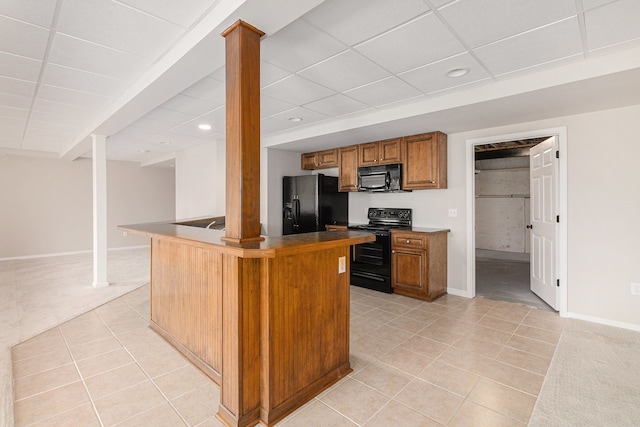 kitchen featuring brown cabinetry, baseboards, light tile patterned floors, and black appliances