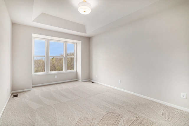 spare room with baseboards, light colored carpet, a tray ceiling, and visible vents