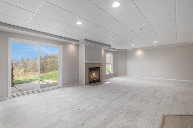 unfurnished living room with baseboards, a drop ceiling, light carpet, and a fireplace