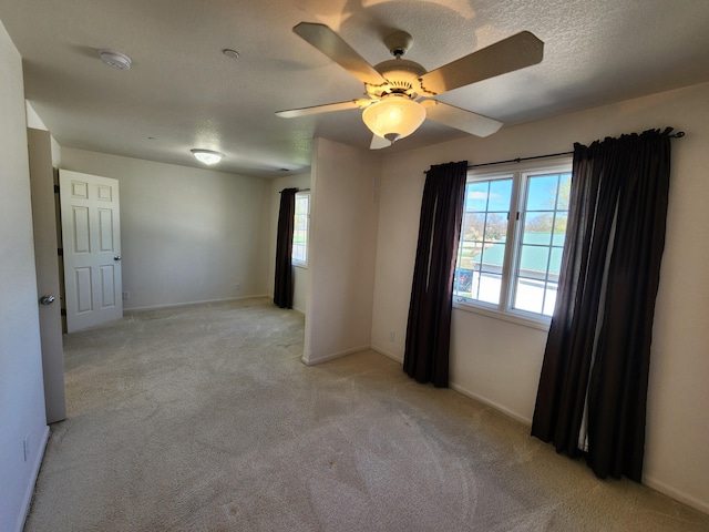 unfurnished room with a ceiling fan, baseboards, light carpet, and a textured ceiling