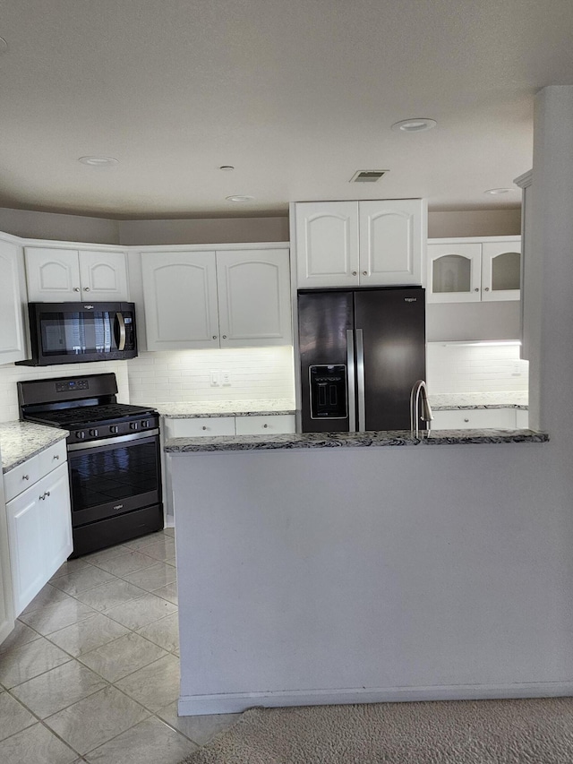 kitchen with white cabinets, black microwave, light stone counters, stainless steel gas stove, and refrigerator with ice dispenser