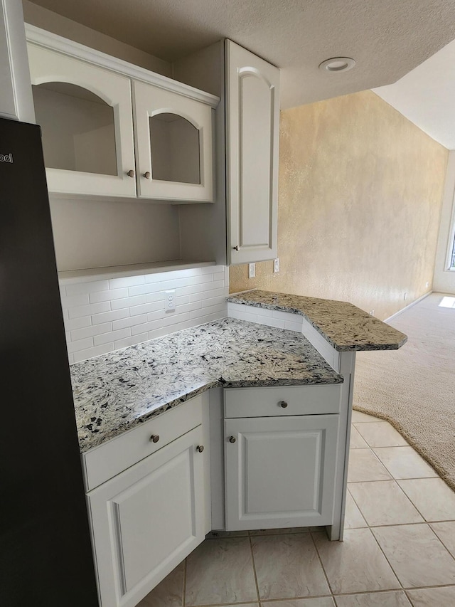 kitchen with backsplash, white cabinetry, light stone countertops, and a textured ceiling