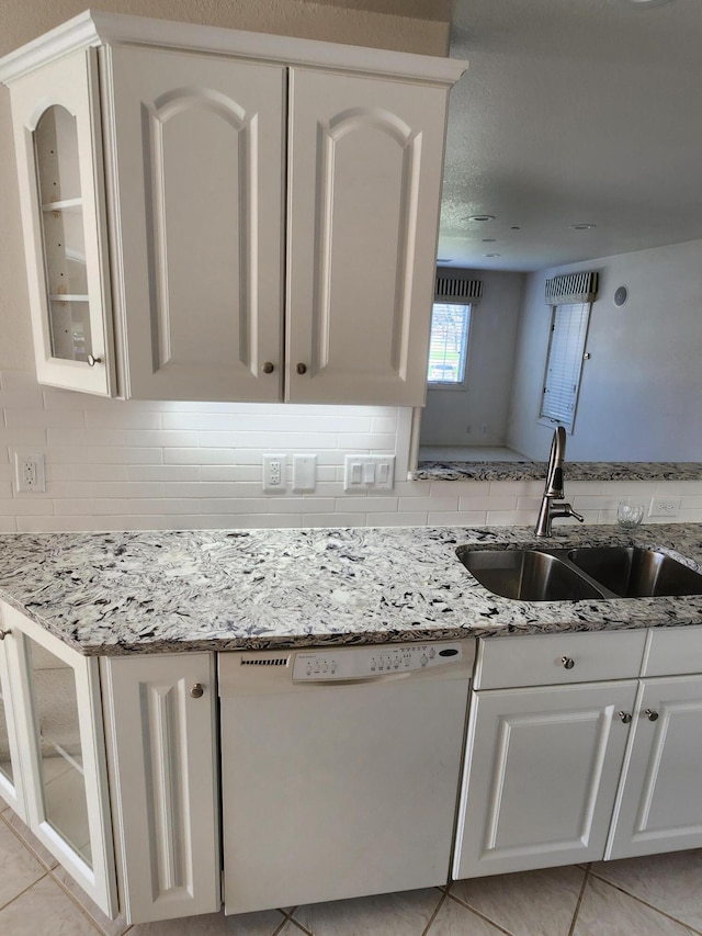 kitchen with light stone countertops, a sink, dishwasher, backsplash, and glass insert cabinets