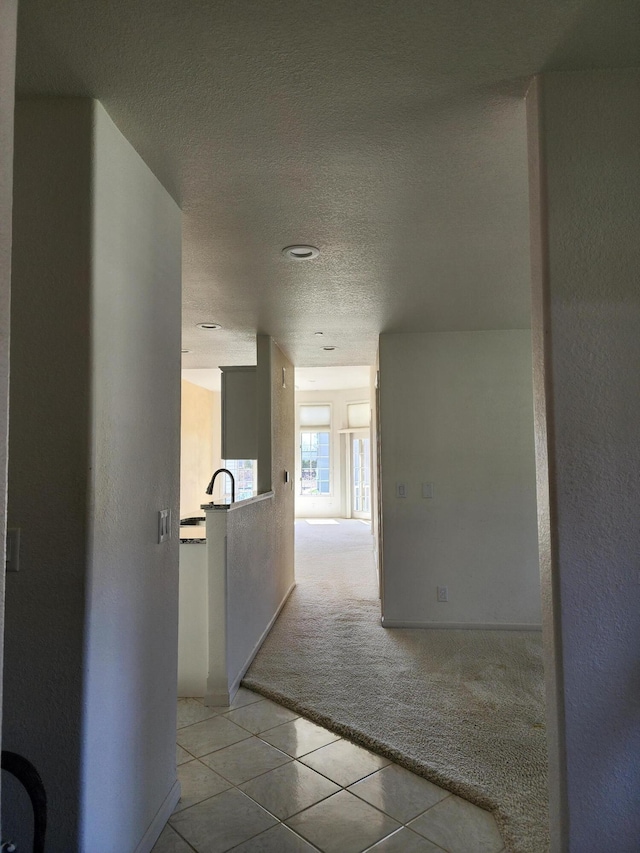 hall featuring light colored carpet, a textured ceiling, and light tile patterned floors