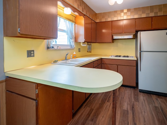 kitchen with a peninsula, white appliances, dark wood-type flooring, light countertops, and a sink