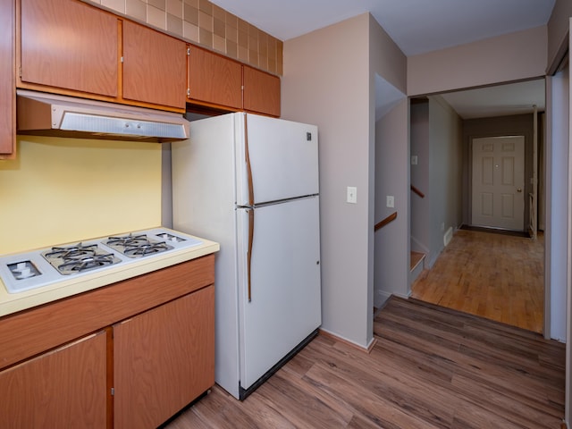 kitchen featuring wood finished floors, light countertops, under cabinet range hood, and white appliances