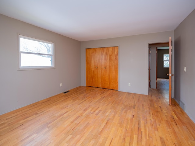 unfurnished bedroom featuring visible vents, light wood finished floors, and a closet