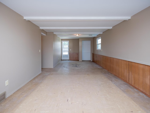 unfurnished room with baseboards, wood walls, wainscoting, and beamed ceiling