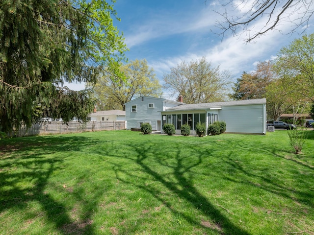 back of property with a yard, fence, a chimney, and a sunroom