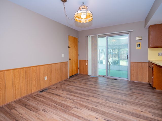 unfurnished dining area featuring wood walls, visible vents, light wood-style flooring, and a wainscoted wall