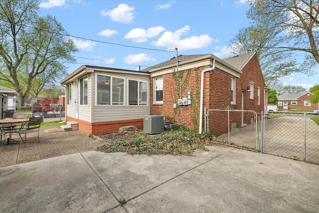view of property exterior with fence, central AC, brick siding, a gate, and a patio area