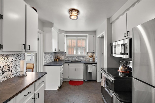 kitchen featuring decorative backsplash, dark countertops, white cabinetry, a sink, and stainless steel appliances