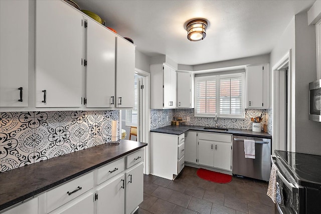 kitchen with dark countertops, white cabinets, a sink, appliances with stainless steel finishes, and backsplash