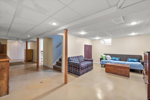 living area with finished concrete flooring, baseboards, a drop ceiling, stairway, and recessed lighting