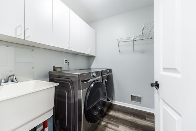 washroom featuring cabinet space, a sink, washing machine and dryer, visible vents, and dark wood-style floors