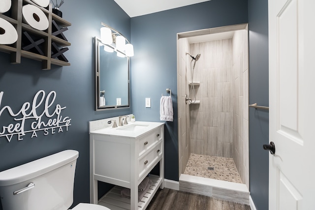 full bathroom featuring vanity, a tile shower, toilet, and wood finished floors