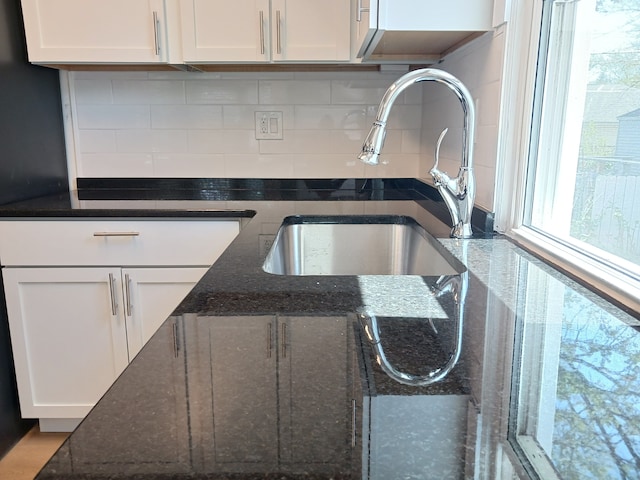 details featuring a sink, tasteful backsplash, dark stone countertops, and white cabinetry