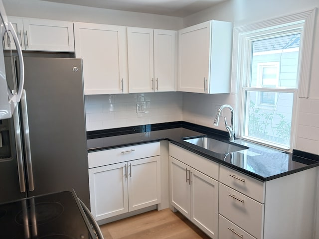 kitchen featuring stainless steel fridge, a sink, backsplash, and white cabinets