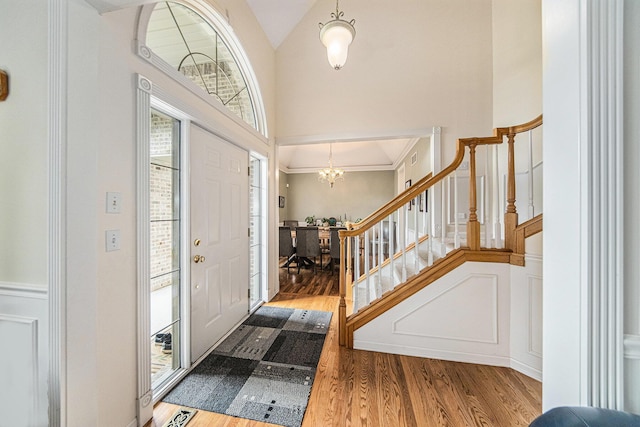 entryway with high vaulted ceiling, stairs, wood finished floors, and a chandelier