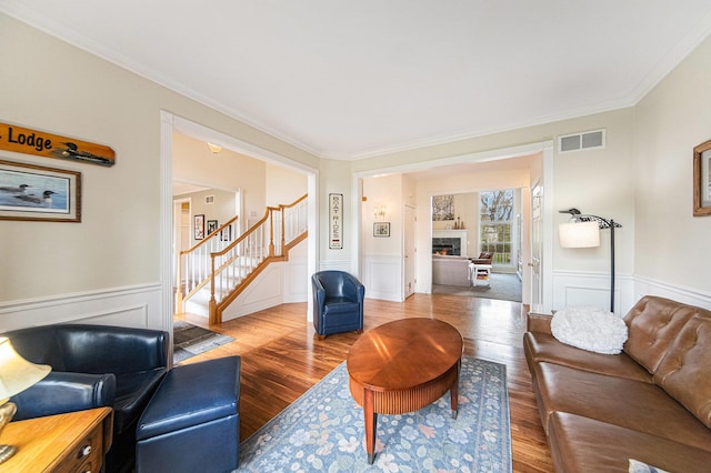 living area featuring crown molding, visible vents, wainscoting, and stairway