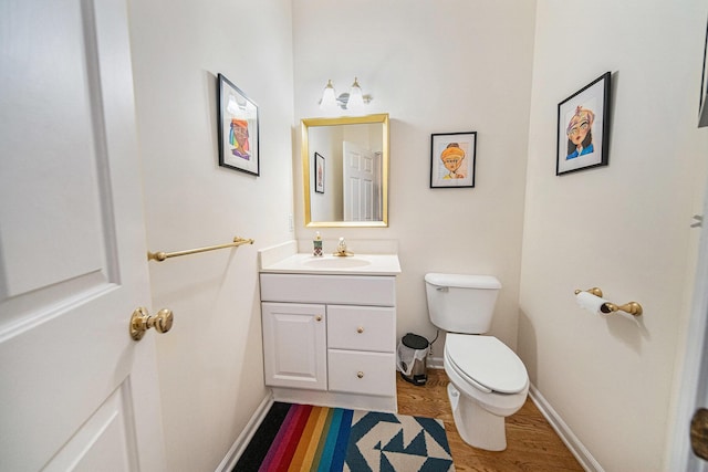 half bathroom featuring toilet, baseboards, wood finished floors, and vanity