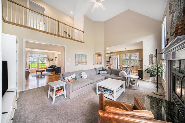 carpeted living area with a high end fireplace, high vaulted ceiling, and a ceiling fan