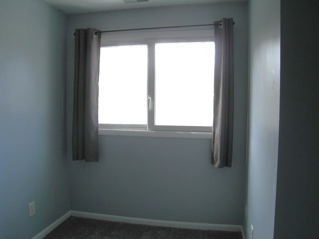 spare room with baseboards, plenty of natural light, and dark carpet
