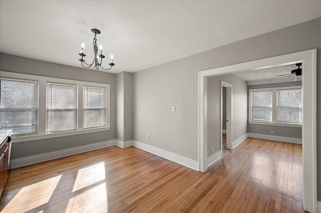 unfurnished dining area featuring baseboards, light wood finished floors, and ceiling fan with notable chandelier
