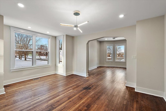interior space featuring arched walkways, baseboards, a wealth of natural light, and hardwood / wood-style flooring