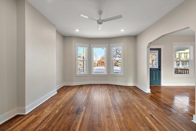 empty room with wood finished floors, baseboards, recessed lighting, arched walkways, and a ceiling fan