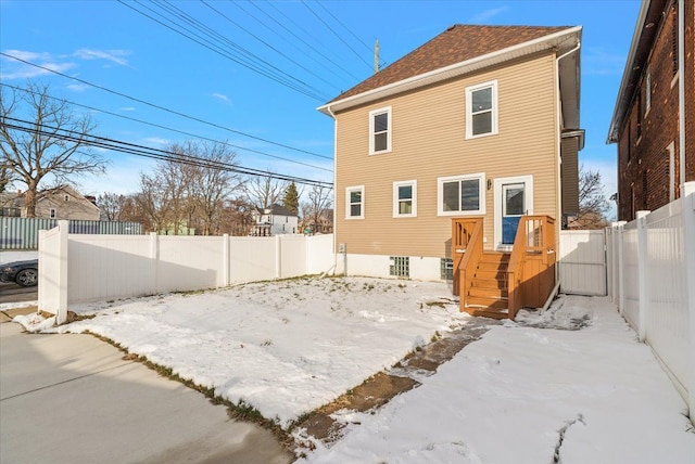 snow covered house with a fenced backyard and roof with shingles