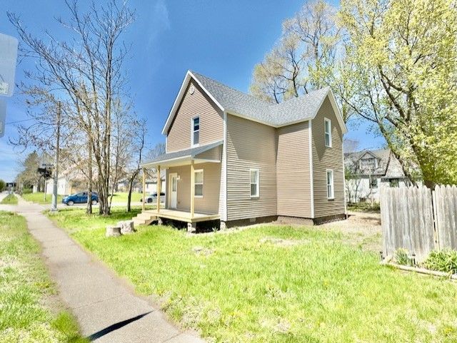 view of side of home with a yard, fence, and covered porch