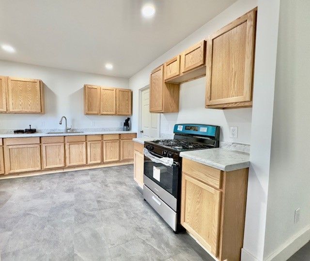 kitchen featuring light brown cabinets, stainless steel range with gas cooktop, recessed lighting, light countertops, and a sink