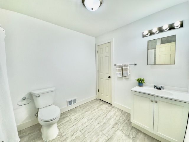 full bath featuring baseboards, vanity, toilet, and visible vents