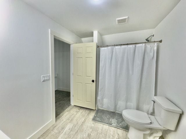 bathroom featuring a shower with curtain, toilet, wood finished floors, and visible vents