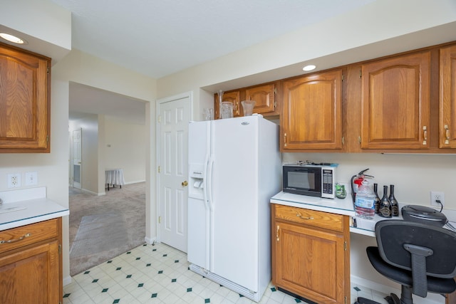kitchen featuring light countertops, white refrigerator with ice dispenser, brown cabinets, and built in study area