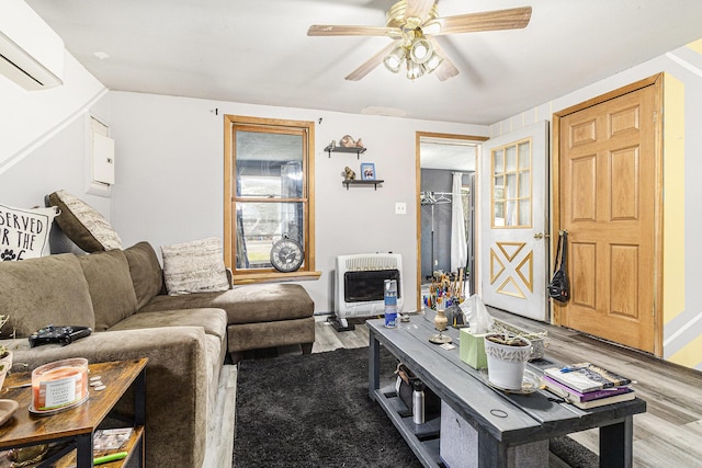 living area with a ceiling fan, heating unit, light wood finished floors, and a wall unit AC