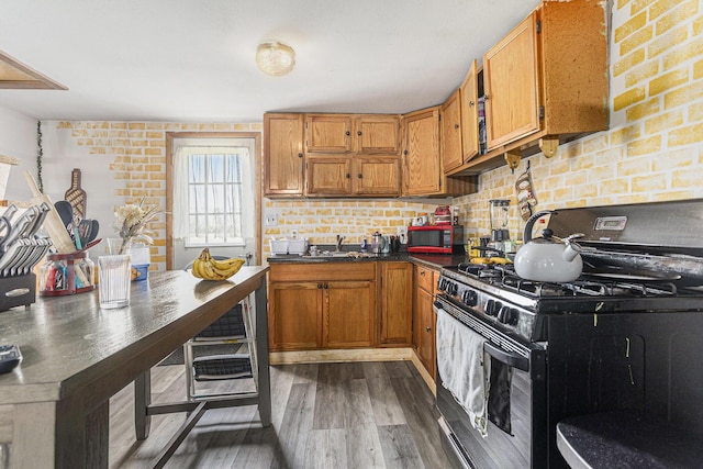 kitchen with dark countertops, black gas range oven, brown cabinetry, tasteful backsplash, and dark wood-type flooring
