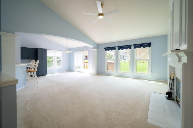 unfurnished living room with light colored carpet, arched walkways, vaulted ceiling, ceiling fan with notable chandelier, and a glass covered fireplace