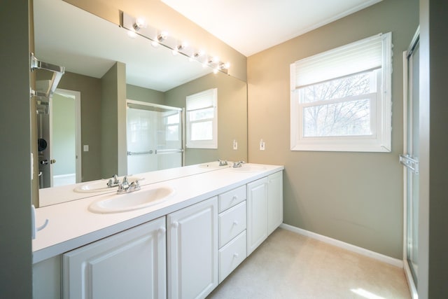 full bathroom featuring double vanity, baseboards, a sink, and a shower with shower door