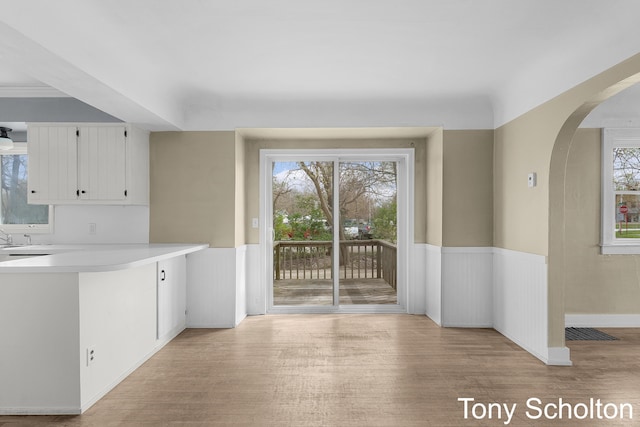 interior space with arched walkways, light wood-type flooring, a wealth of natural light, and a wainscoted wall
