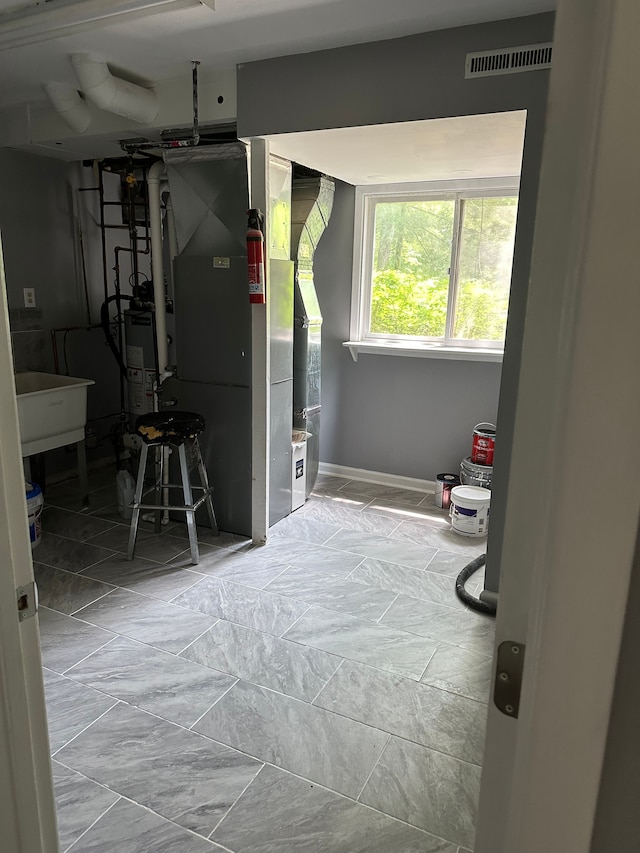 basement featuring heating unit, a sink, gas water heater, visible vents, and baseboards